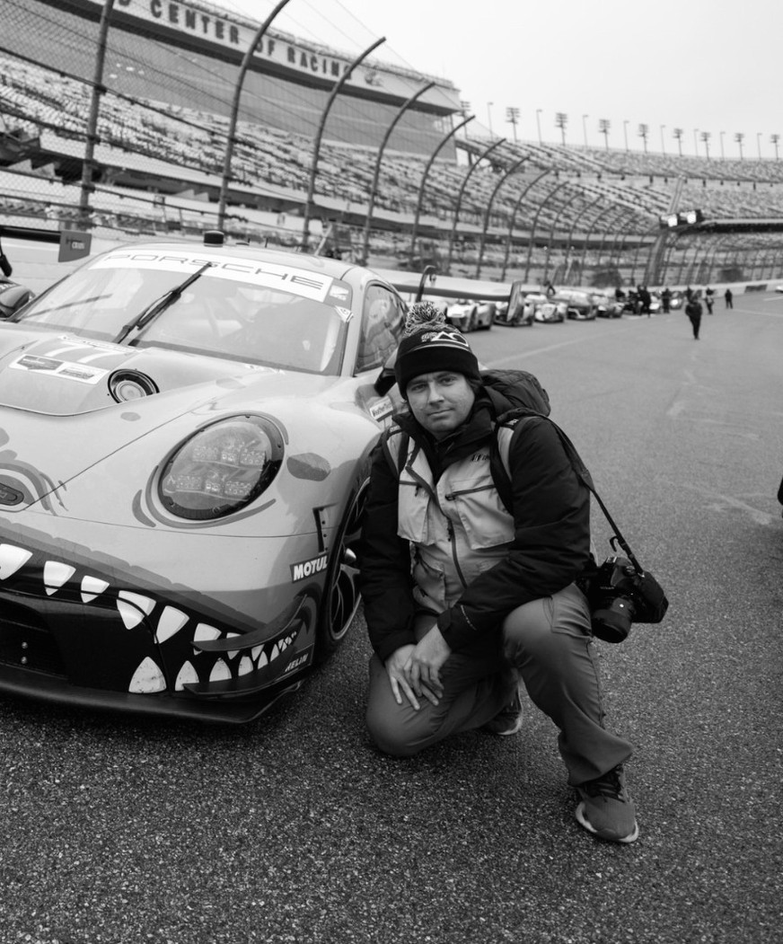 Camden Thrasher accroupi à côté de la Porsche d'AO Racing sur la piste de Daytona, un appareil photo à l'épaule
