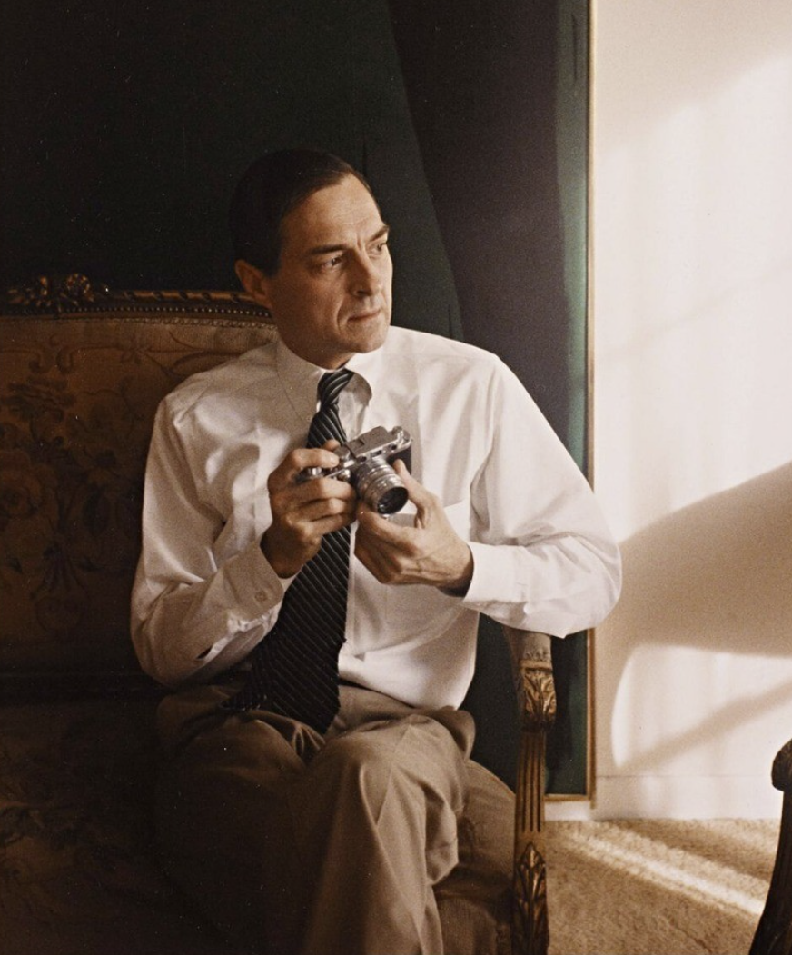 William Eggleston assis dans un fauteuil, un appareil photo télémétrique dans les mains